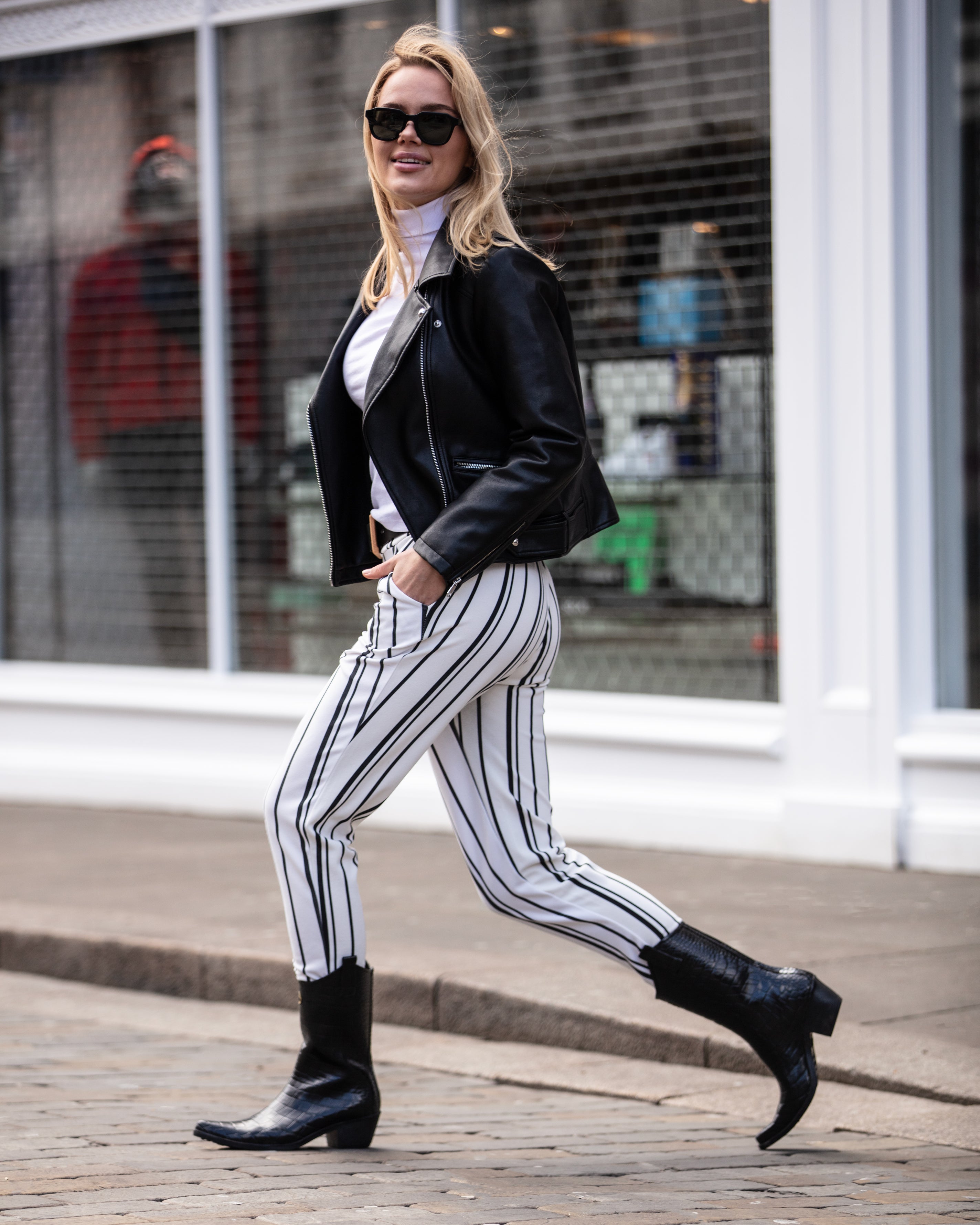 Girl striding across the road in black and whlte stripy trousers wearing Talolo mock croc black cowboy wellies