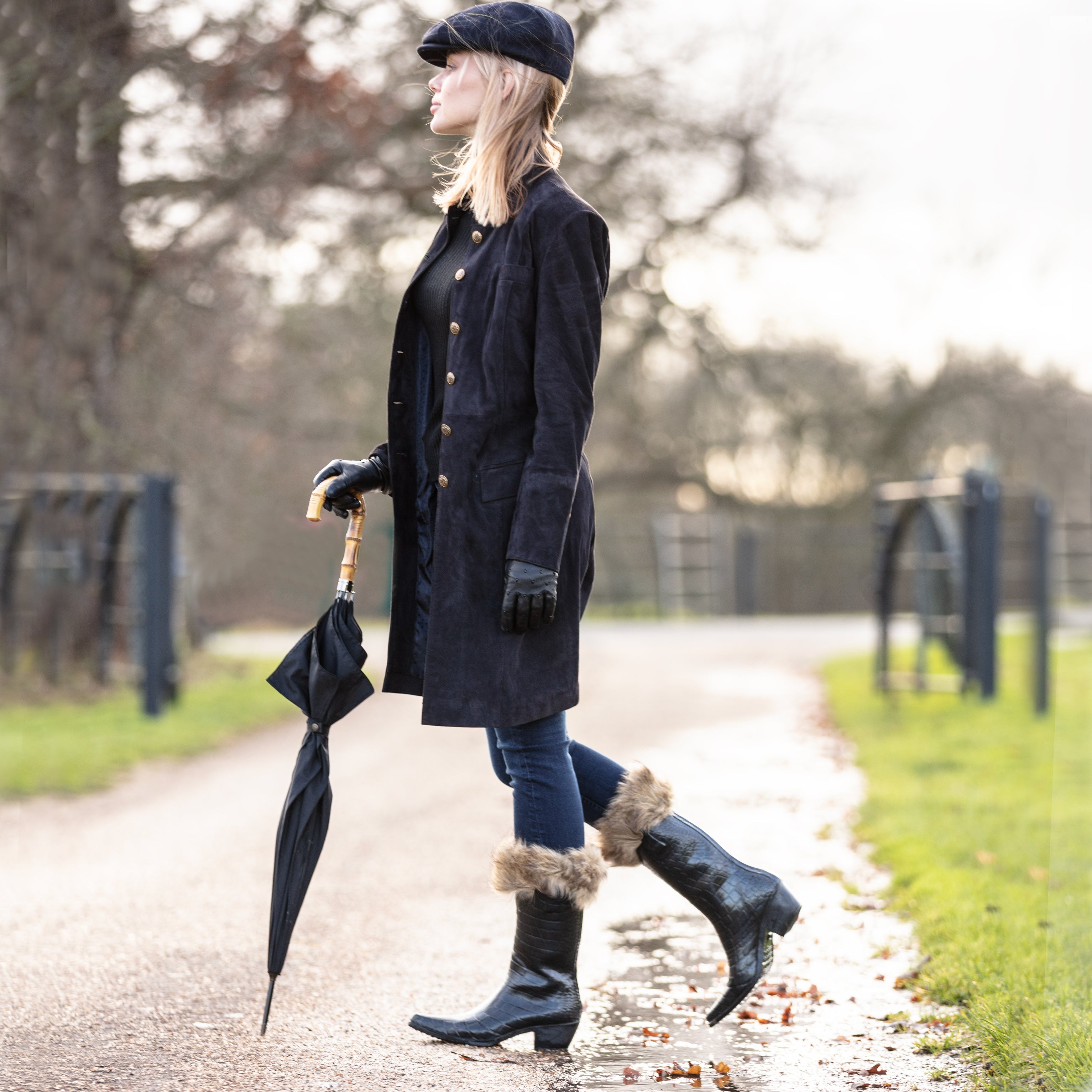 Girl wearing black coat and smart talolo mock croc urban cowboy boot wellies and holding an umbrella