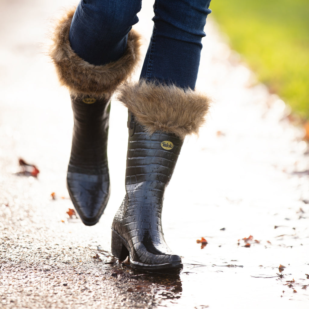 Talolo black mock croc urban wellies walking towards the camera with fur lined top on a wet road
