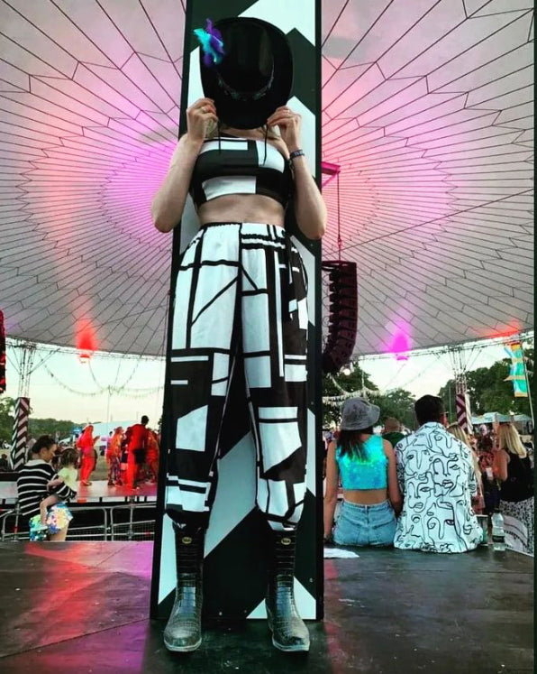 lady at a festival wearing geometric black and white trousers and top  with a black hat in front of her face and wearing Black Talolo cowboy boot wellies