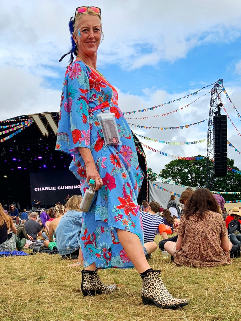girl at festival with stage in background wearing a blue flowery dress and Leopard print cowboy ankle welly boots