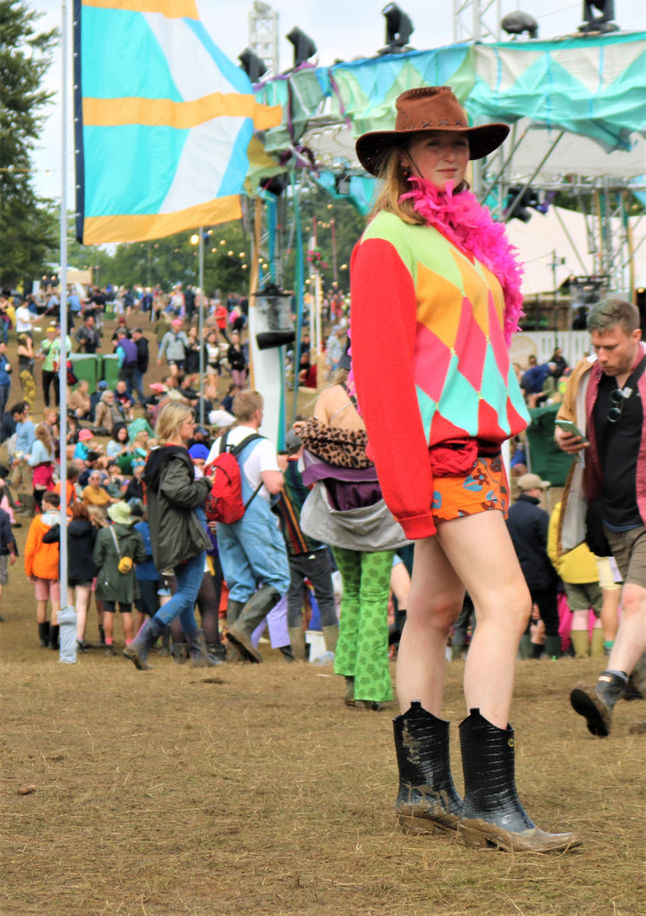 Girl at festival wearing bright coloured geometric jumper, feather bower and black Talolo Boots , mock croc cowboy boot wellies 
