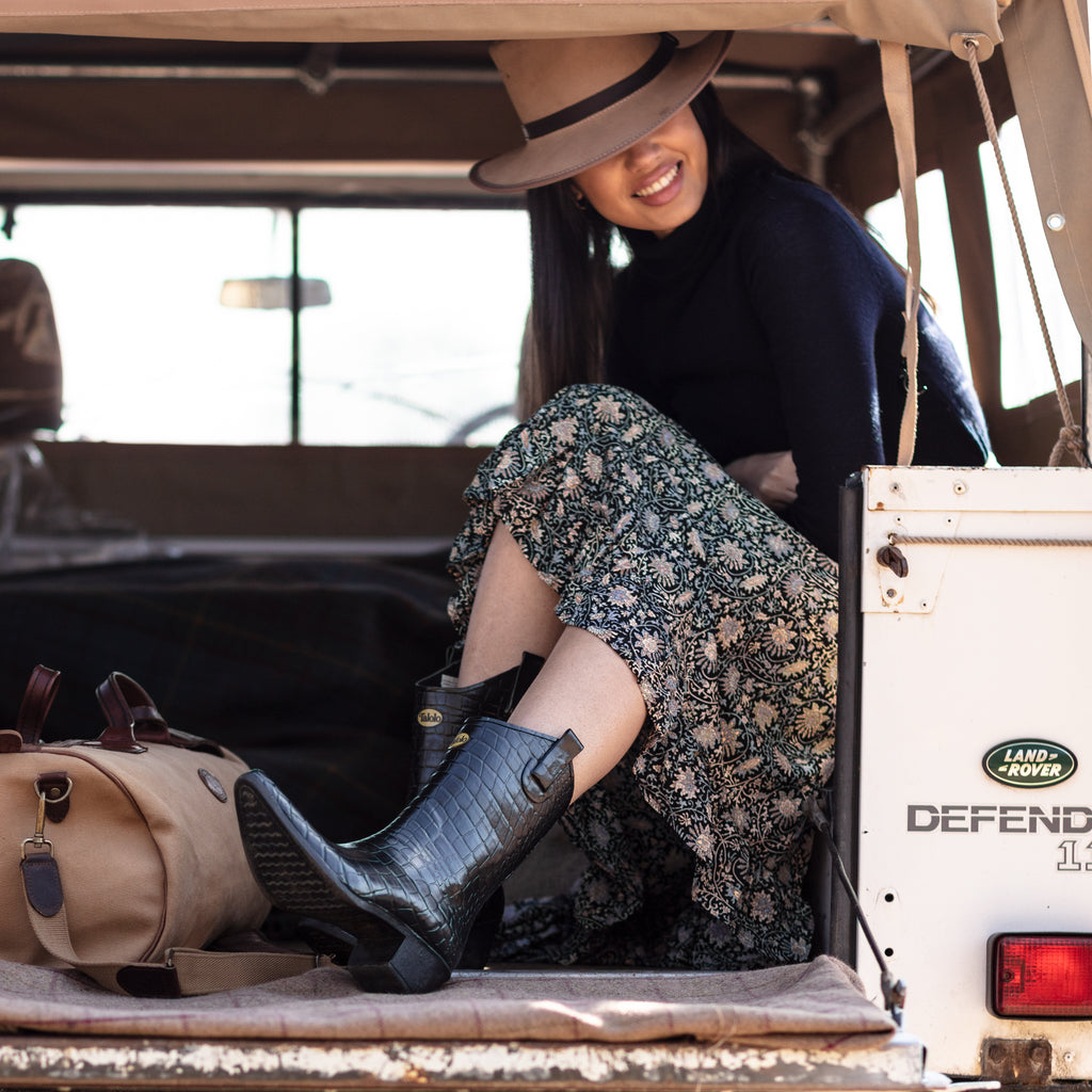 Girl sitting in the back of a landrover with hat and skirt wearing Talolo black super stylish cowboy wellies