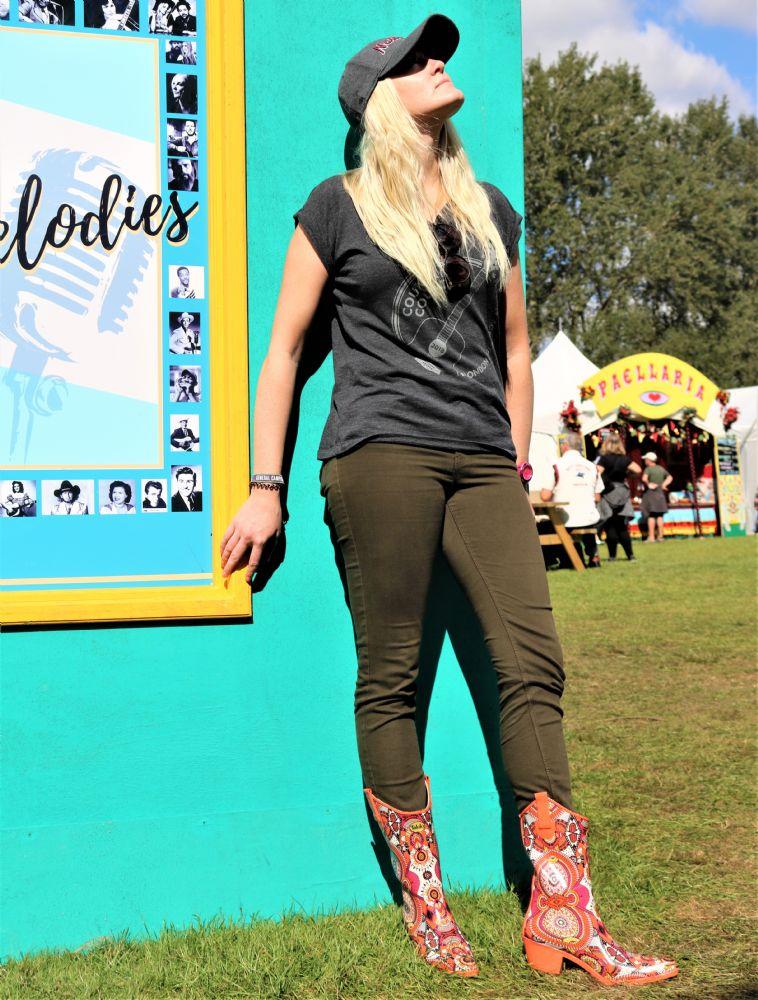 Girl in funky orange cowboy wellies leaning against a turquoise wall at a festival